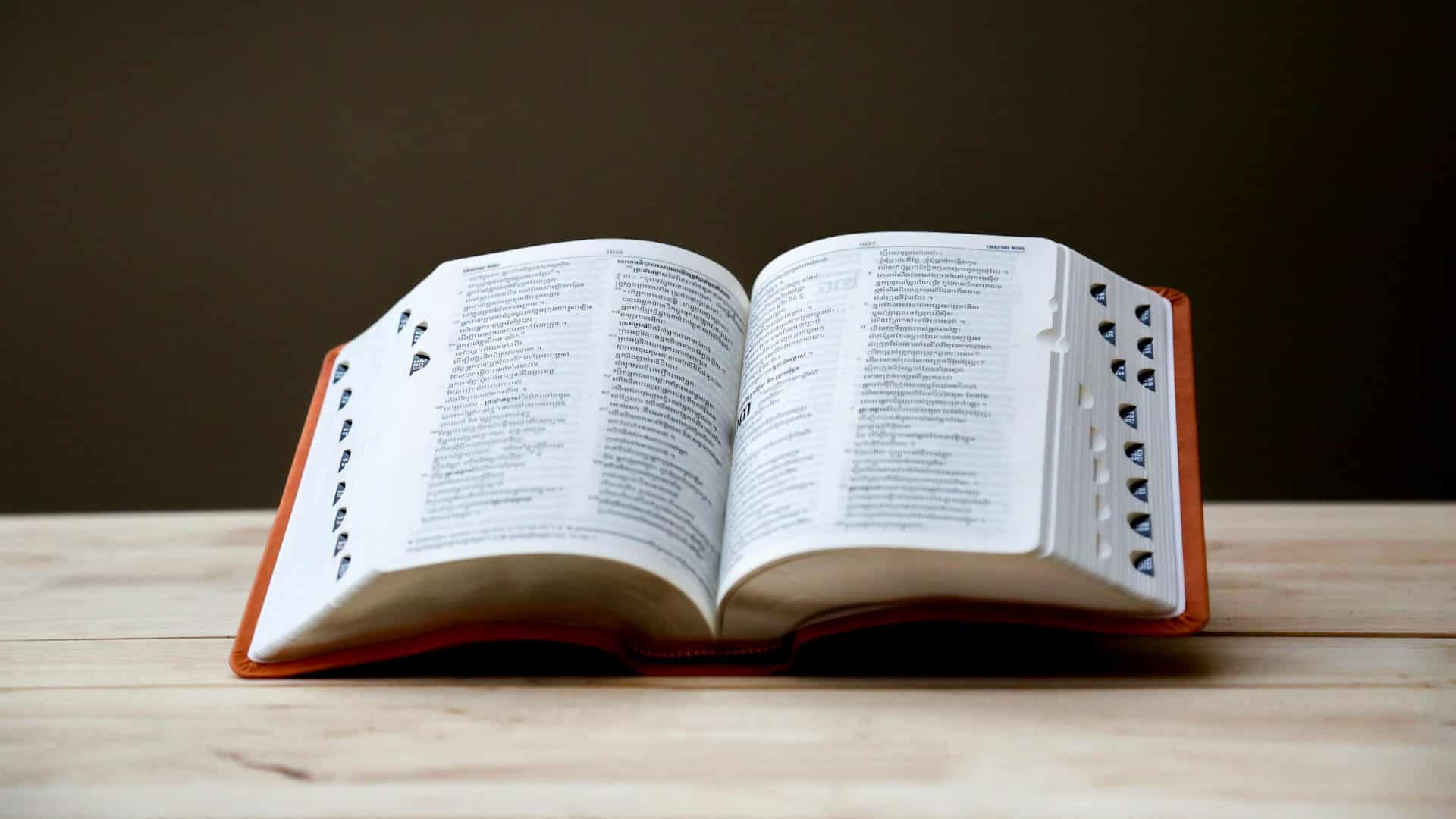 An open Bible resting on a pale wooden table