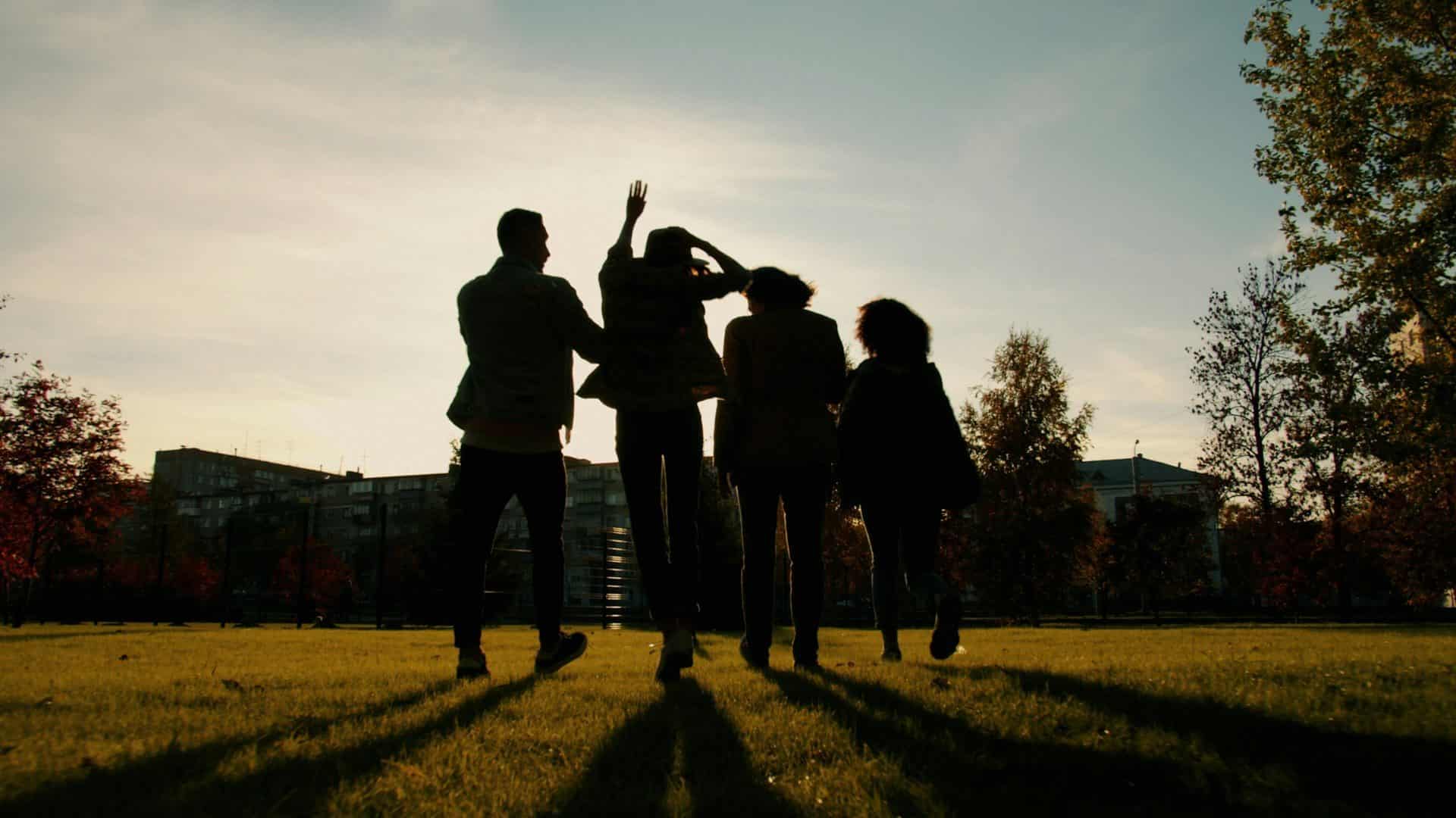 Four silhouettes walking through a park at sunset